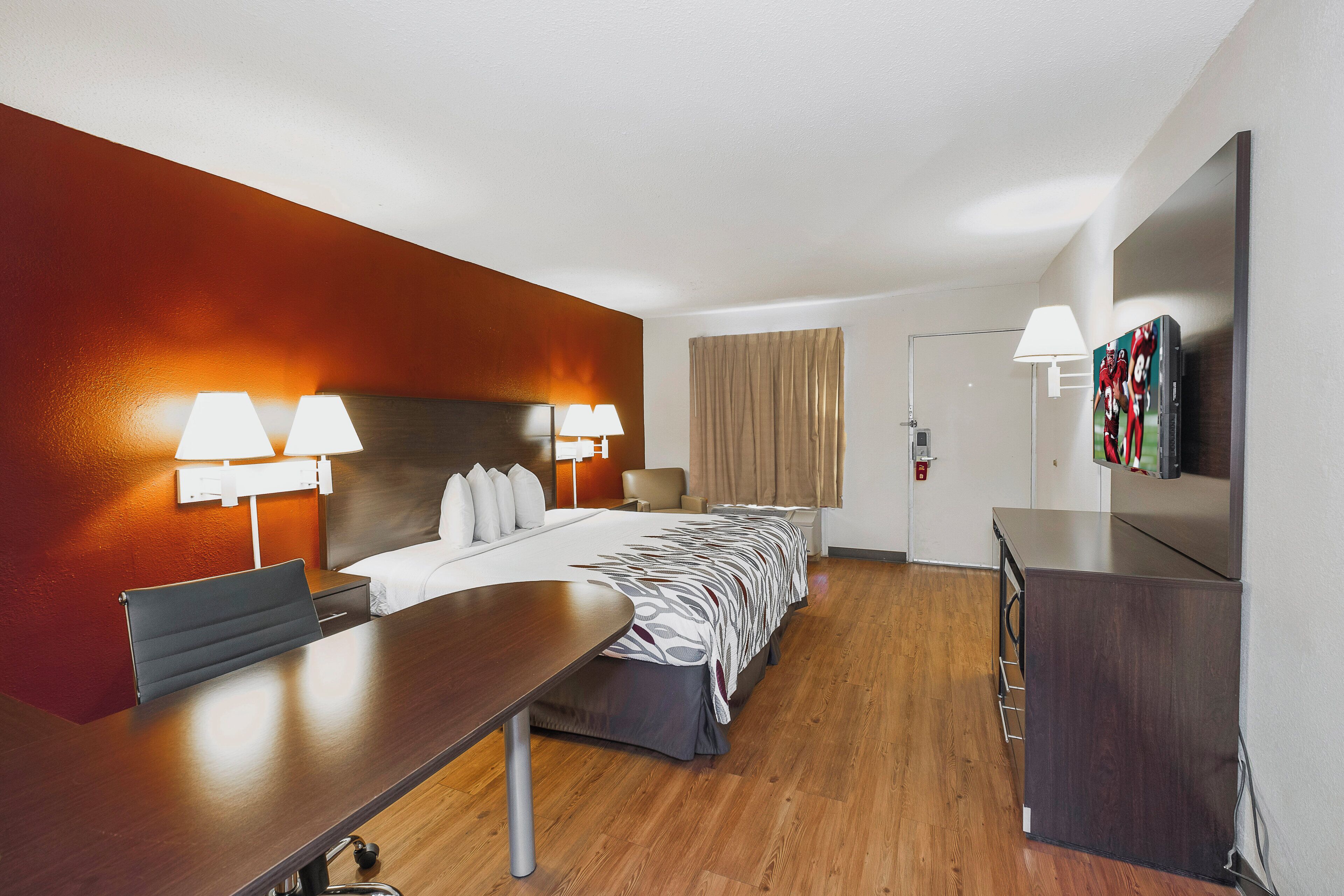 Una habitación de hotel con una cama, un escritorio, dos lámparas, un televisor y una puerta.
