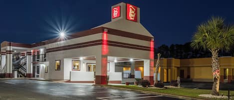 Un hotel con fachada roja y blanca, un estacionamiento y una palmera.