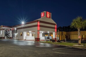 Een hotel met een gevel in rood en wit, een parkeerplaats en een palmboom.
