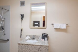 A bathroom with a shower, a hairdryer, a sink with a soap dispenser, and a towel rack. - Red Roof Inn Walterboro (Walterboro)