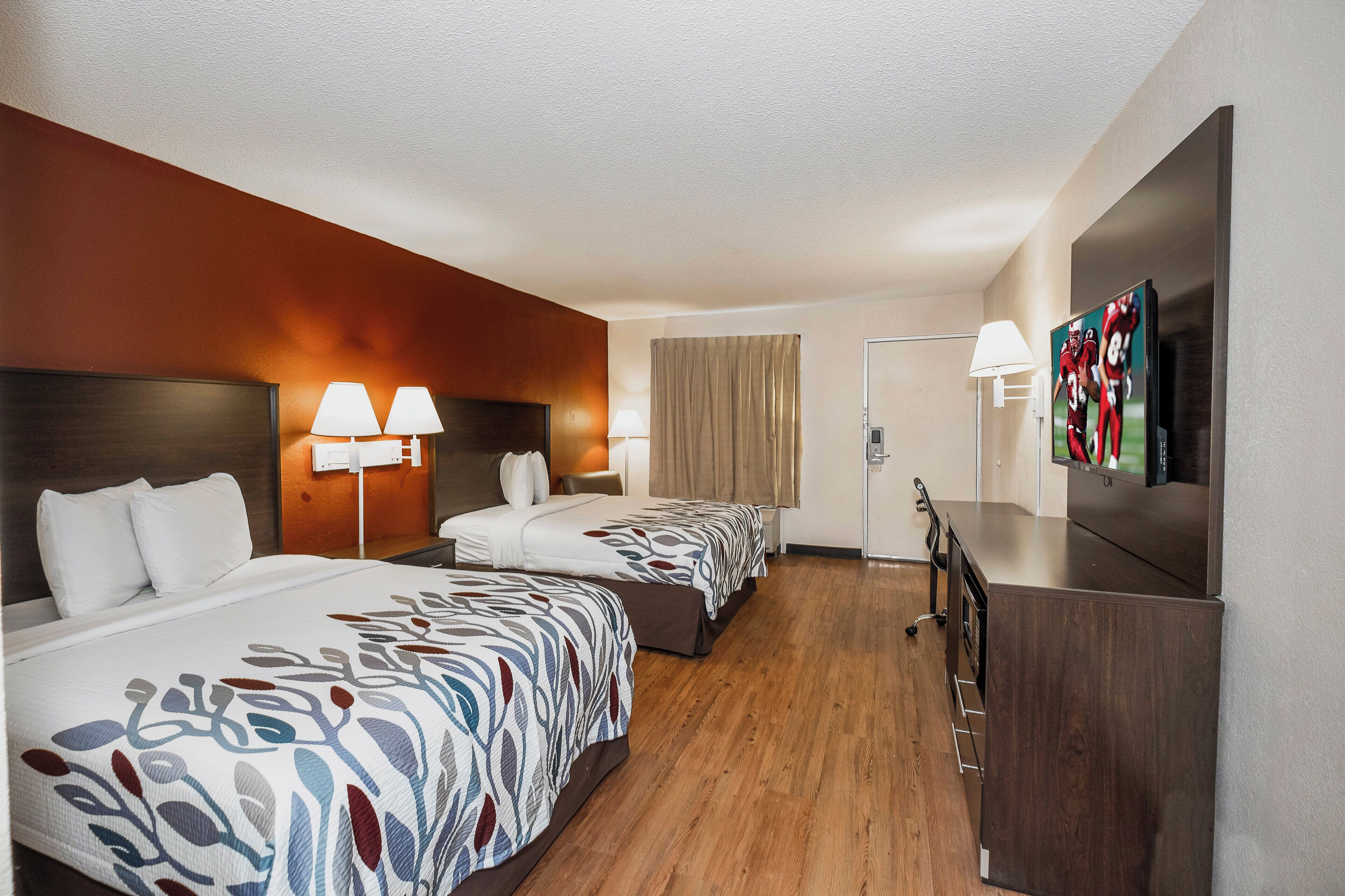 Ein Hotelzimmer mit zwei Betten, einem Schreibtisch, einem Fernseher und einer Badezimmertür.