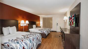 Ein Hotelzimmer mit zwei Betten, einem Schreibtisch, einem Fernseher und einer Badezimmertür.