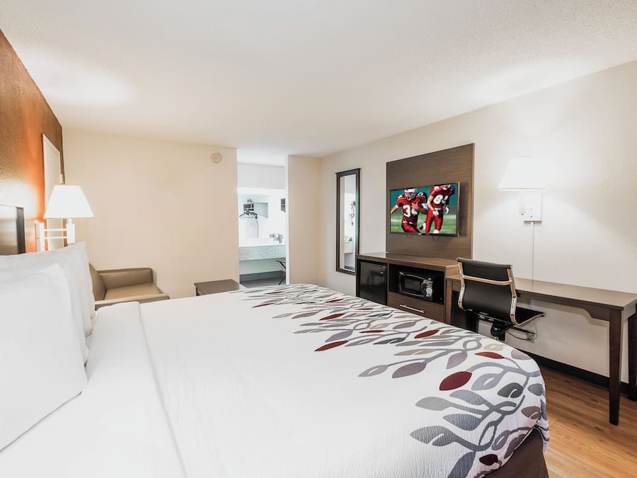 A hotel room with a large bed, a desk, a television, and a view of the bathroom.