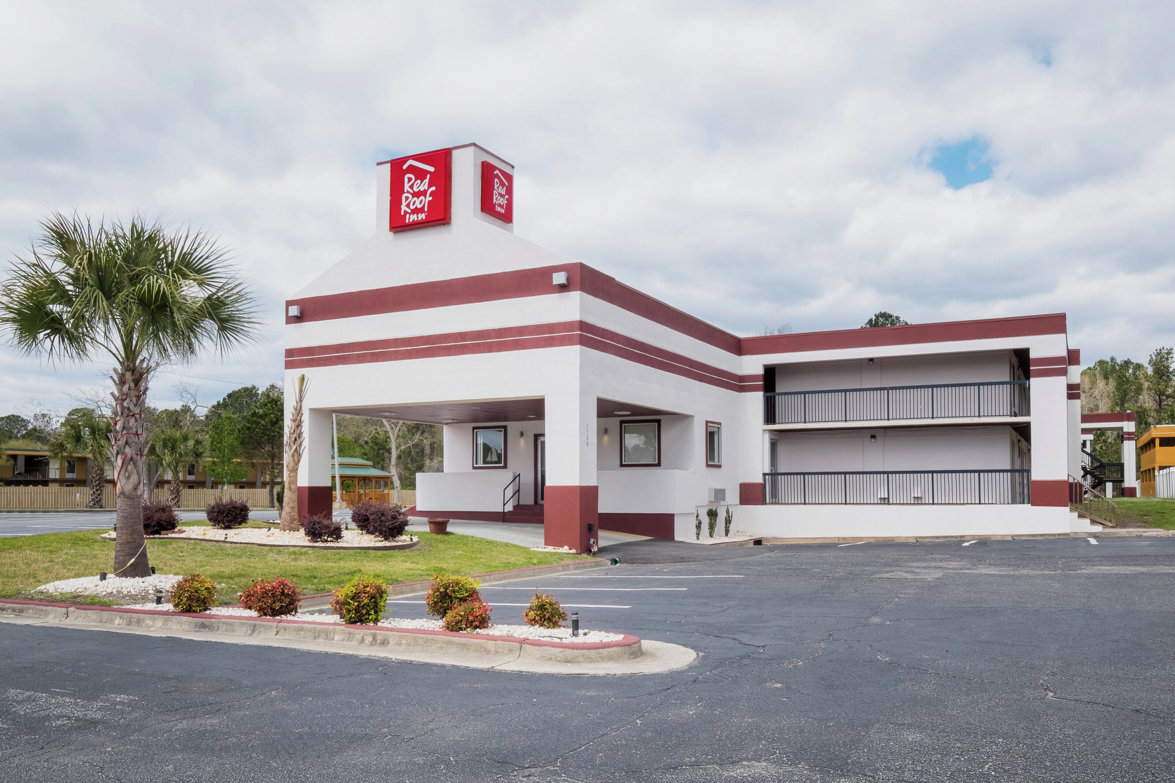 Un hotel Red Roof Inn de dos pisos, con estacionamiento techado y una palmera en primer plano.