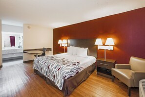A hotel room with a bed, bedside lamps, a chair, a desk, and a mirror. - Red Roof Inn Walterboro (Walterboro)