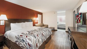 A hotel room with a large bed, a bedside table, a lamp, a seating area with a chair, and a television. - Red Roof Inn Walterboro (Walterboro)