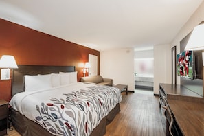 A hotel room with a large bed, a bedside table, a lamp, a seating area with a chair, and a television. - Red Roof Inn Walterboro (Walterboro)