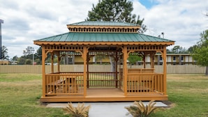 A wooden gazebo with a green roof, surrounded by a grassy area and a wooden fence. - Red Roof Inn Walterboro (Walterboro)