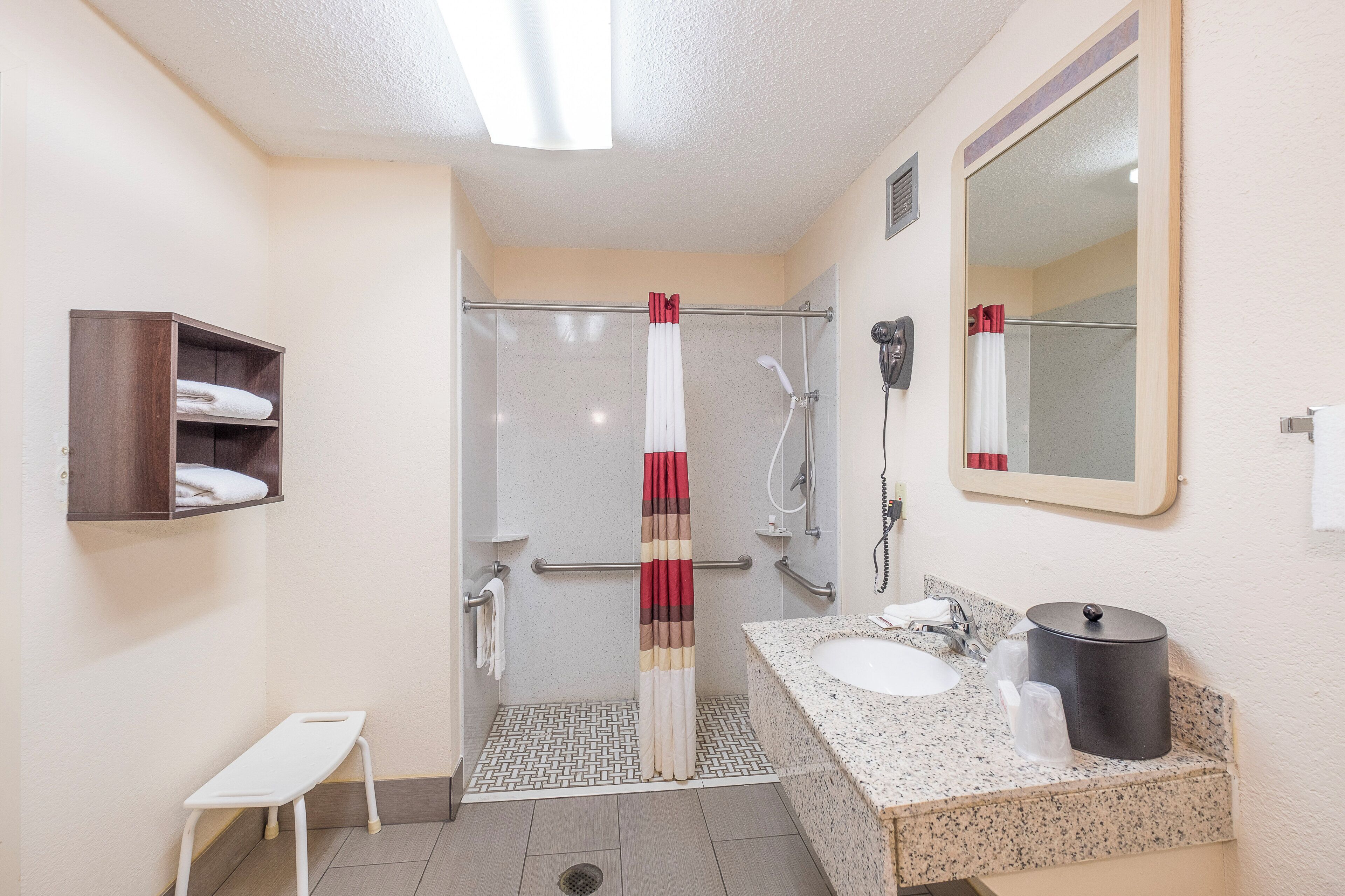 Ein Badezimmer mit Dusche, Waschbecken, Spiegel, Handtuchhalter und einer kleinen Bank.