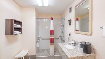 Ein Badezimmer mit Dusche, Waschbecken, Spiegel, Handtuchhalter und einer kleinen Bank.