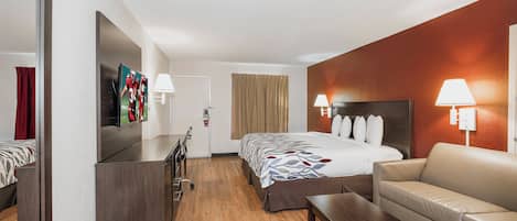 A hotel room with a bed, a desk, a chair, a sofa, and a TV.