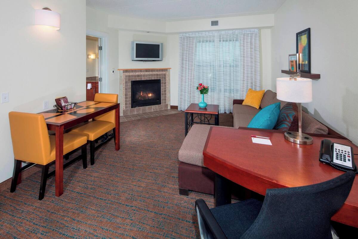 Habitación de hotel con mesa de comedor, sillas, sofá, televisor, chimenea y lámpara.