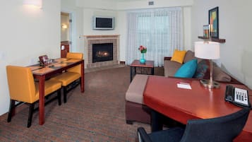 A hotel room with a dining table, chairs, a sofa, a TV, a fireplace, and a lamp.