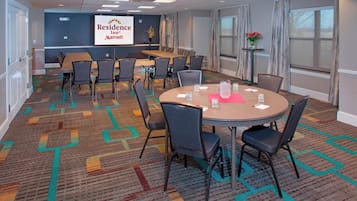 A conference room with a large table and chairs, a projector screen with the Residence Inn logo, and a carpeted floor.