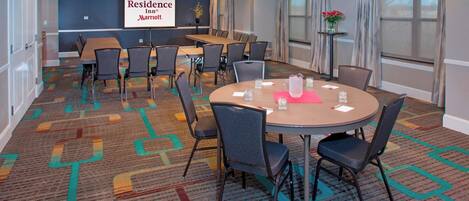 A conference room with a large table and chairs, a projector screen with the Residence Inn logo, and a carpeted floor.