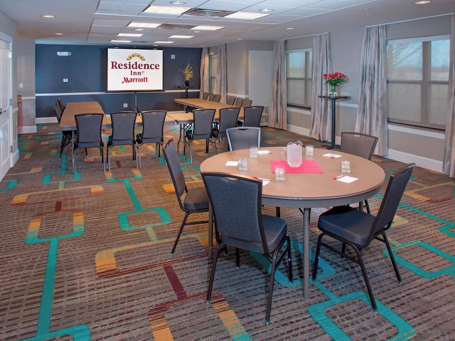 Una sala de conferencias con una gran mesa y sillas, una pantalla para proyector con el logotipo de Residence Inn, y piso alfombrado.