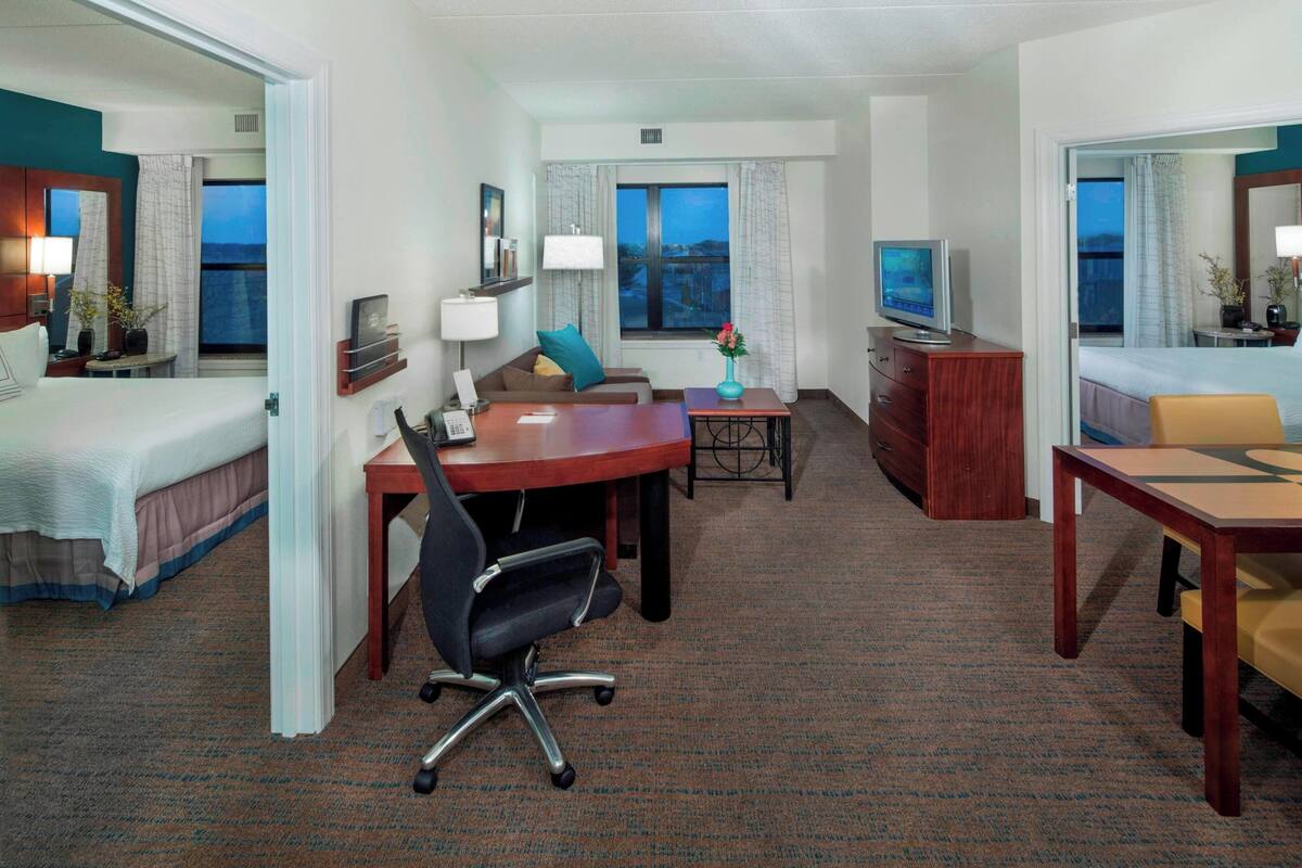 Habitación de hotel con cama, escritorio, silla, televisor y ventana con cortinas.