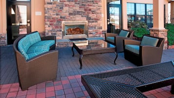An outdoor patio with wicker furniture, a glass-top table, and a stone wall with a fireplace.