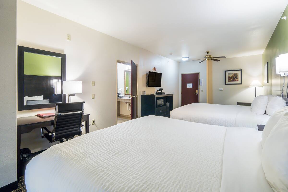 A hotel room with two beds, a desk, a chair, a television, and a ceiling fan.