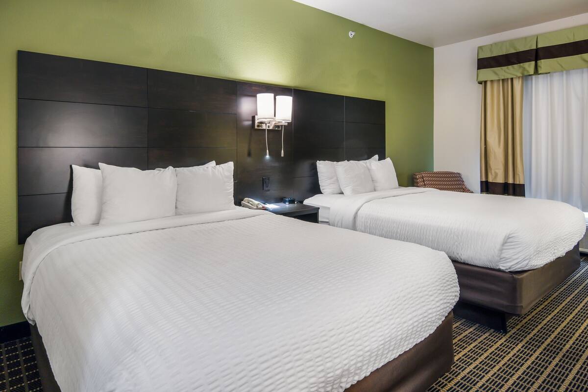 A hotel room with two beds, a headboard, a nightstand, and a chair.