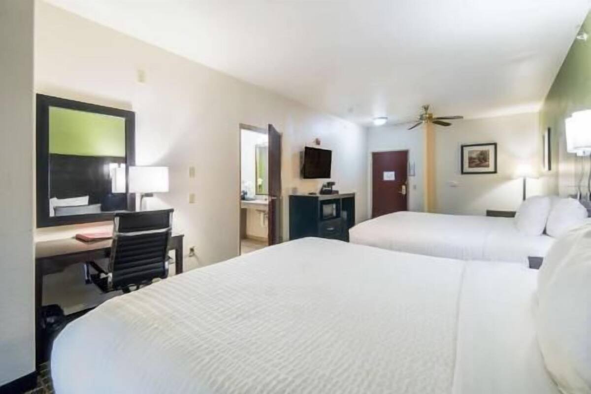 A hotel room with two beds, a desk, a chair, a TV, and a ceiling fan.