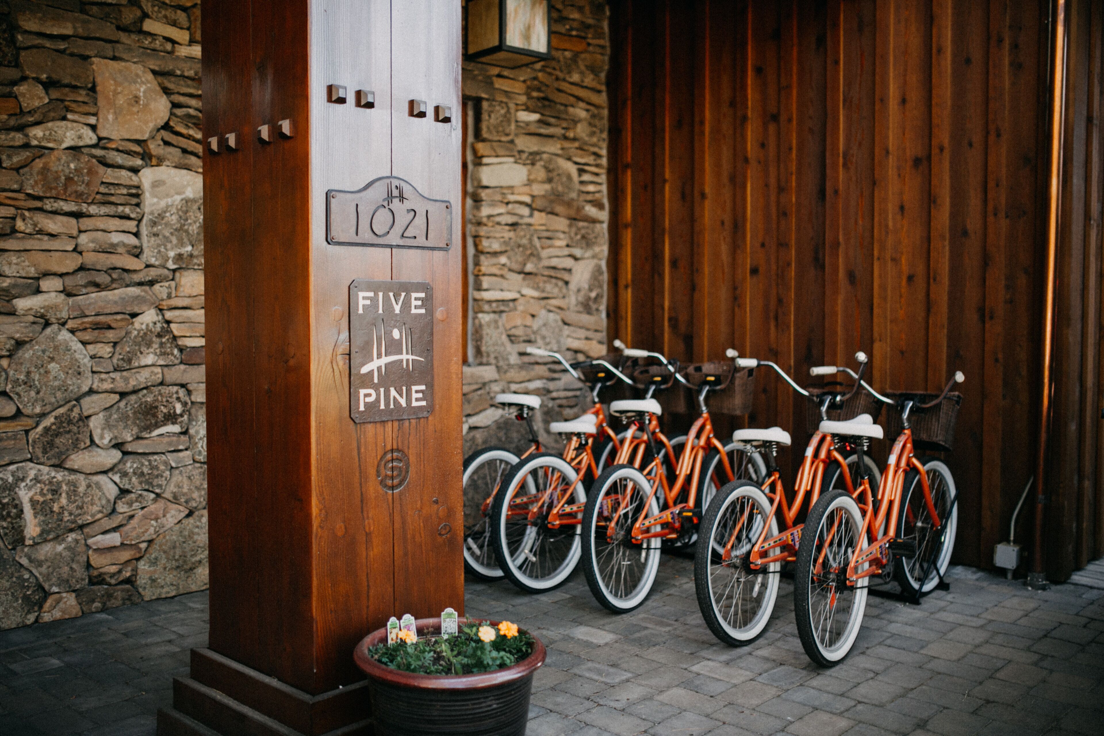 A wooden door with a sign reading "1021 FIVE PINE" and a row of orange bicycles parked outside.