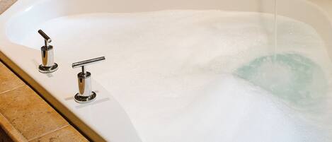 A bathtub with two faucets, a wooden chair, and a fireplace in the background.