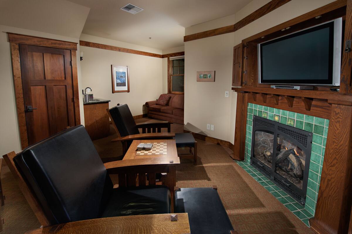 A cozy living room with a fireplace, a television mounted above it, a dining table with chairs, and a sofa.