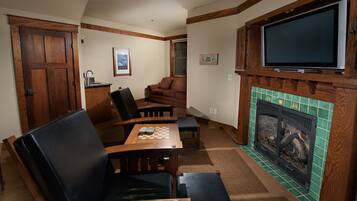 A cozy living room with a fireplace, a television mounted above it, a dining table with chairs, and a sofa.
