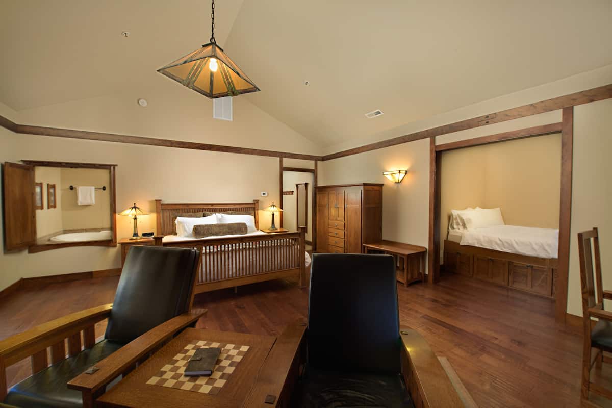 A spacious hotel room with a large bed, a desk with a chessboard, and a seating area with chairs.