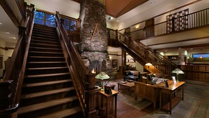 A spacious lobby with a grand staircase, a stone pillar, and a cozy seating area with lamps. - FivePine Lodge & Spa (Sisters)