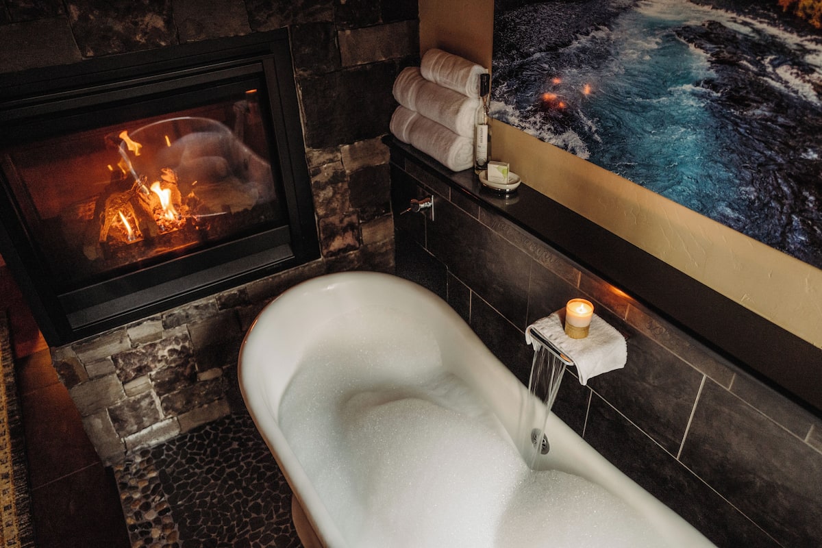 A bathroom with a bathtub, a stone wall, a fireplace, and a painting.