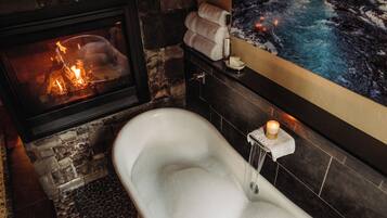A bathroom with a stone wall, a bathtub, a fireplace, and a wall-mounted towel rack.