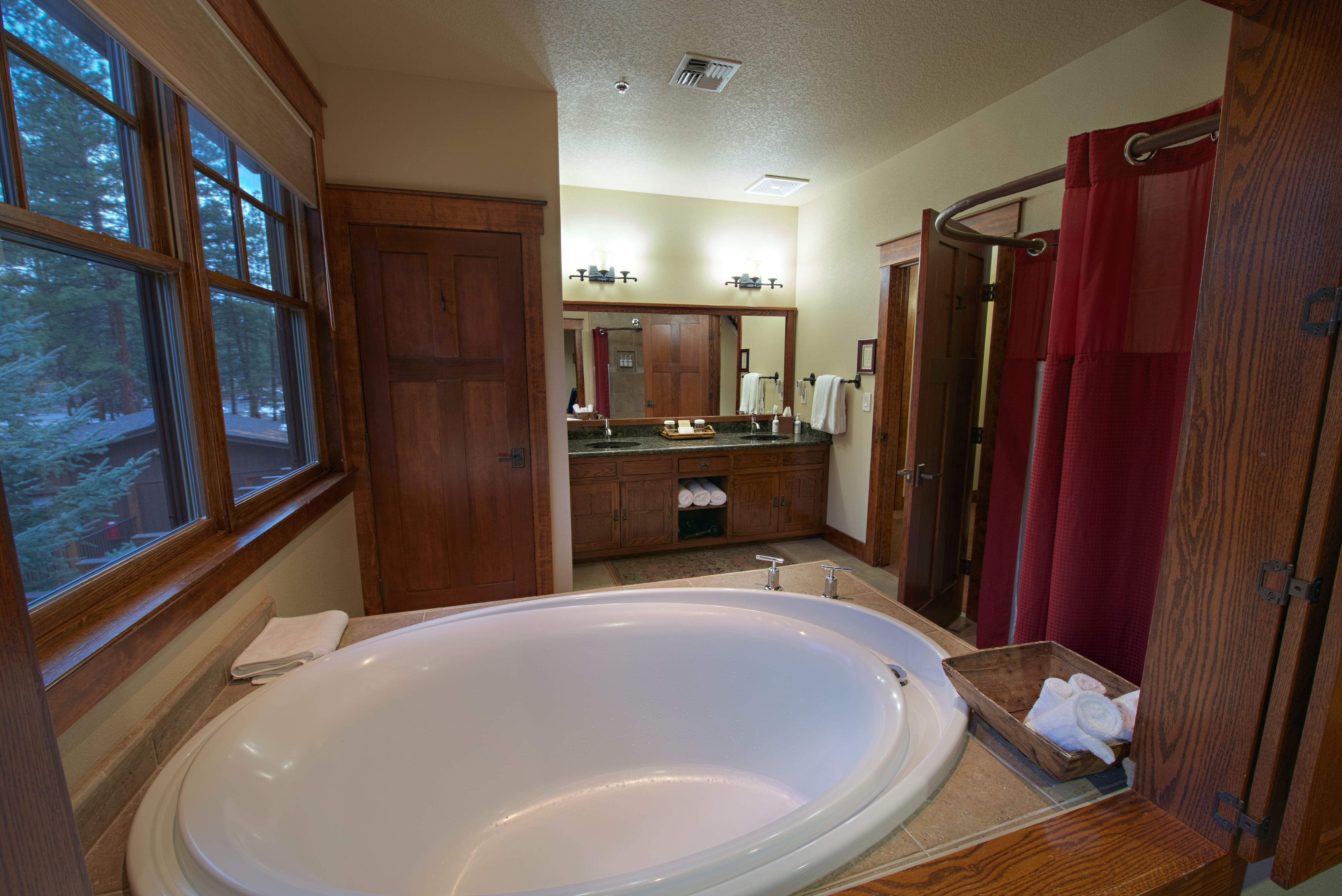 A bathroom with a large bathtub, wooden cabinets, a vanity with a mirror, and a window with a view of trees.