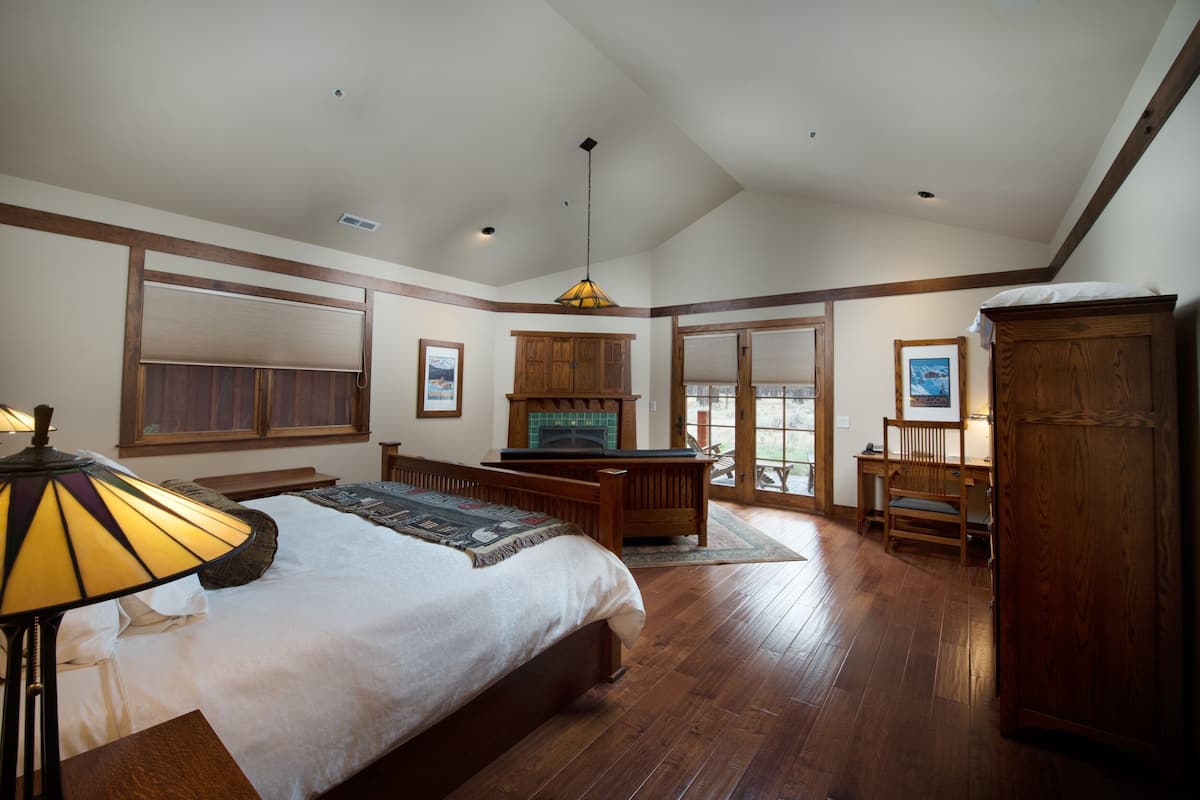 A spacious bedroom with a large bed, wooden flooring, a fireplace, and a desk area.