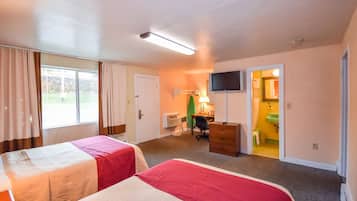 A hotel room with two beds, a desk, a chair, a television, and a bathroom visible through an open door.