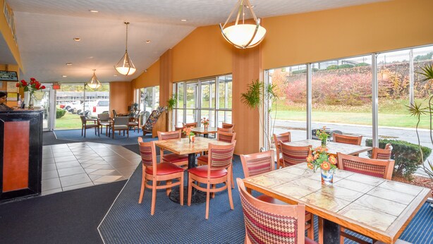 Ein Restaurant mit mehreren Tischen und Stühlen, großen Fenstern und hängenden Lampen.