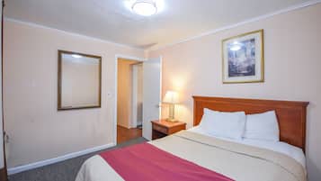Una habitación de hotel con una cama grande, una mesita de noche con lámpara, un cuadro en la pared y una puerta que da a otra habitación.