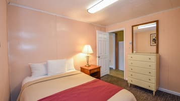 Ein Hotelzimmer mit Bett, Schminktisch, Nachttisch mit Lampe und einer Tür zu einem weiteren Raum.