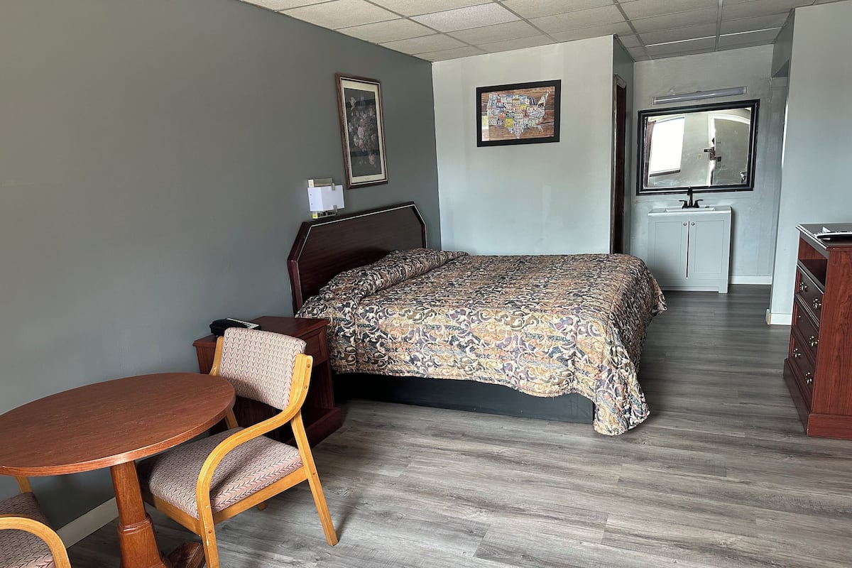 A hotel room with a bed, a desk, a chair, a small table, and a cabinet.