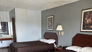 A hotel room with two beds, a wooden floor, a desk with a lamp, and a painting on the wall.