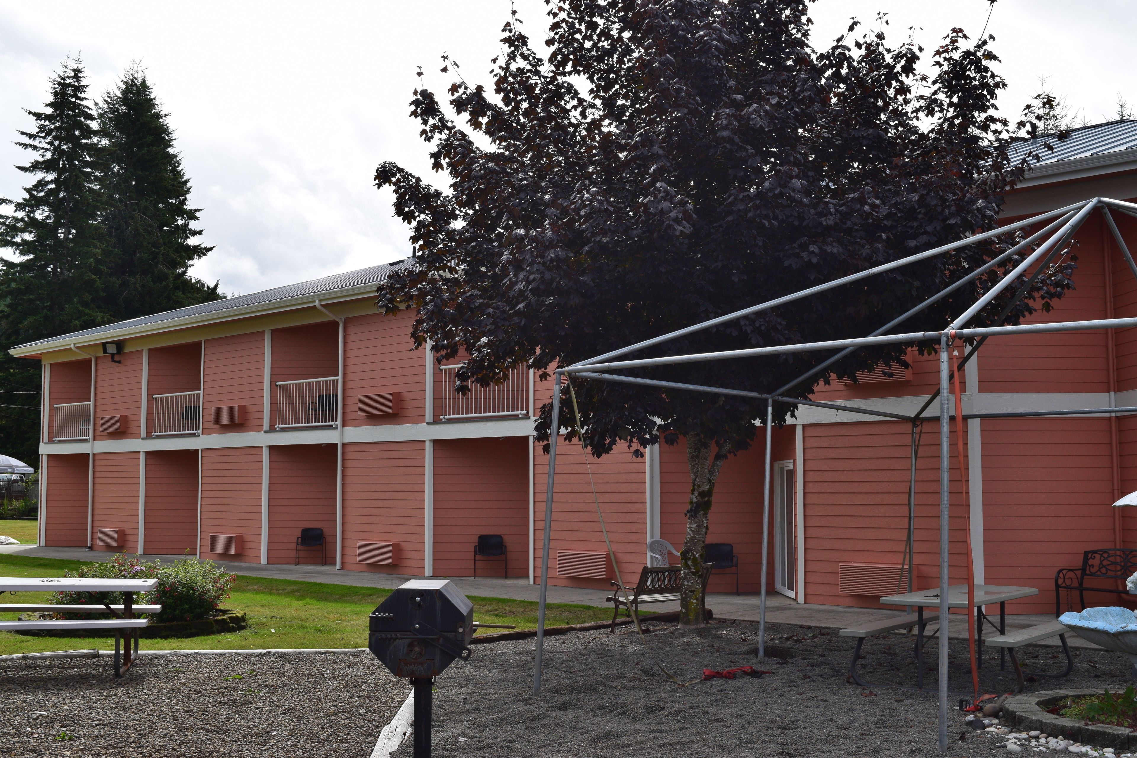 A building with a red exterior, multiple balconies, and a covered outdoor area with tables and chairs.