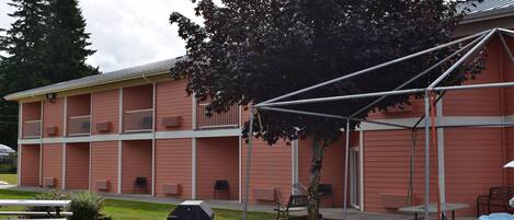 A building with a red exterior, multiple balconies, and a covered outdoor area with tables and chairs.