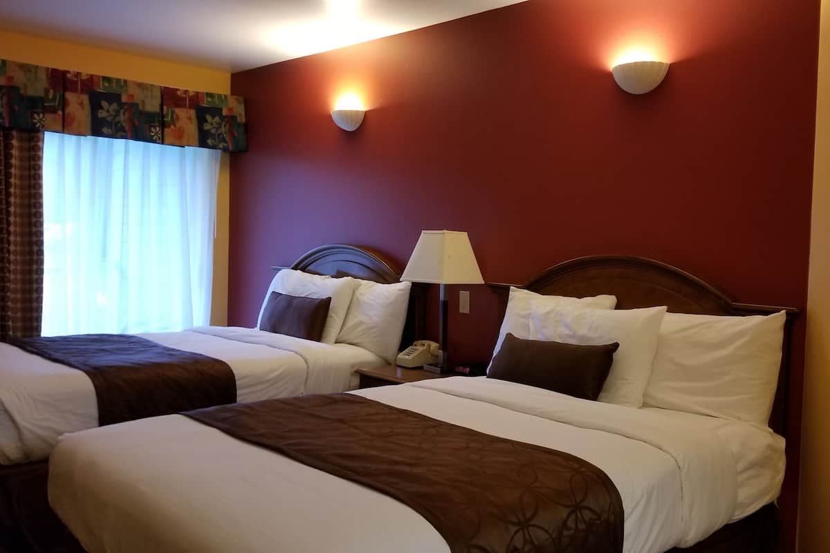 A hotel room with two beds, a telephone, and a lamp.