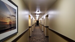 A hotel hallway with a patterned carpet, framed artwork on the walls, and a ceiling light fixture. - The Dew Drop Inn Motel (Forks)