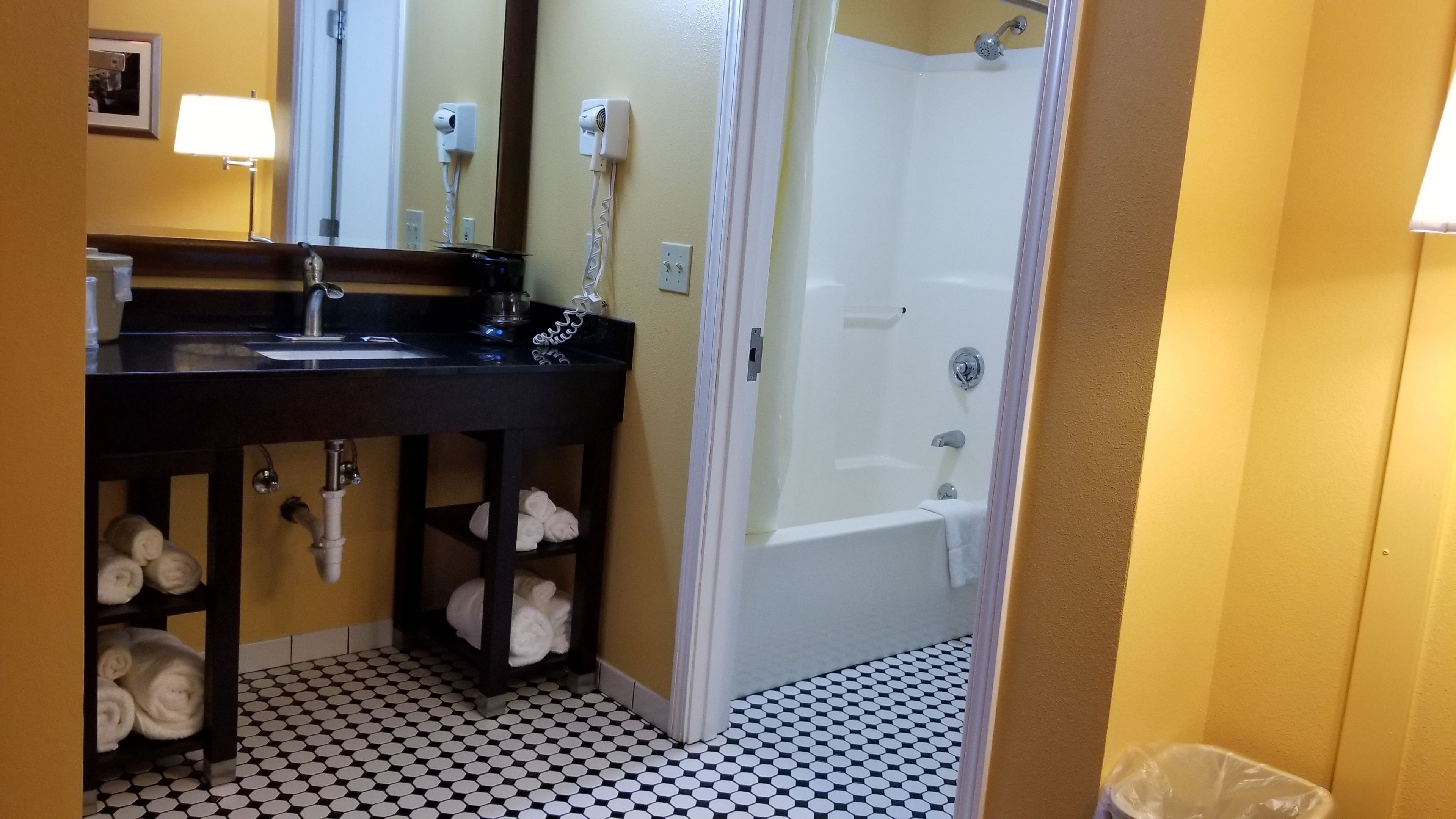 A bathroom with a black sink, mirror, and towel racks. There is a shower area with a bathtub and a toilet.