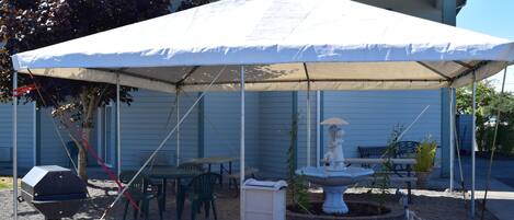 A covered outdoor area with a grill, tables, chairs, and a statue.