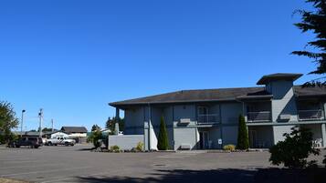 A two-story motel with a parking lot, a small garden, and a clear blue sky.