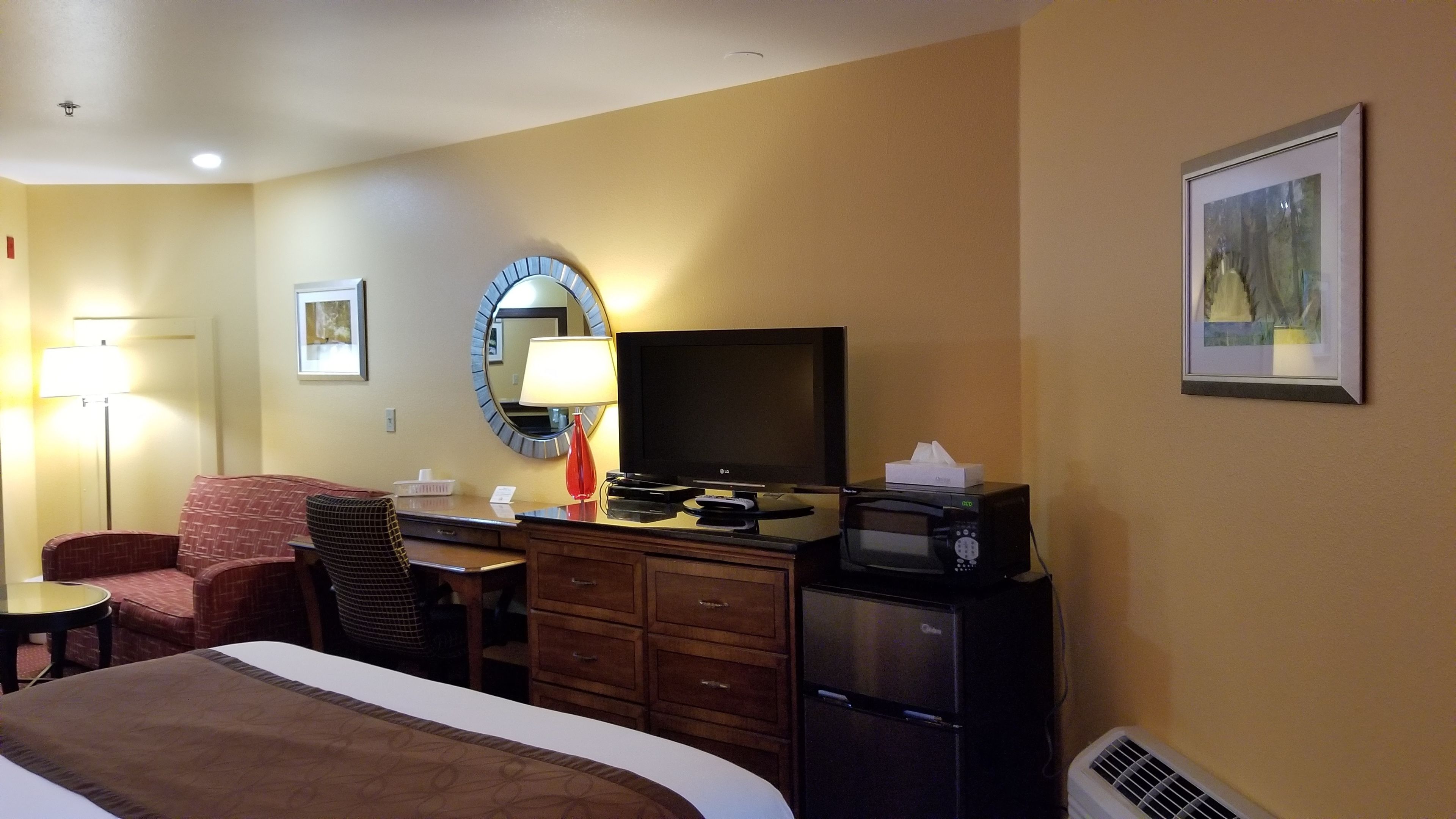 A hotel room with a bed, a desk with a computer, a television, a microwave, and a refrigerator.
