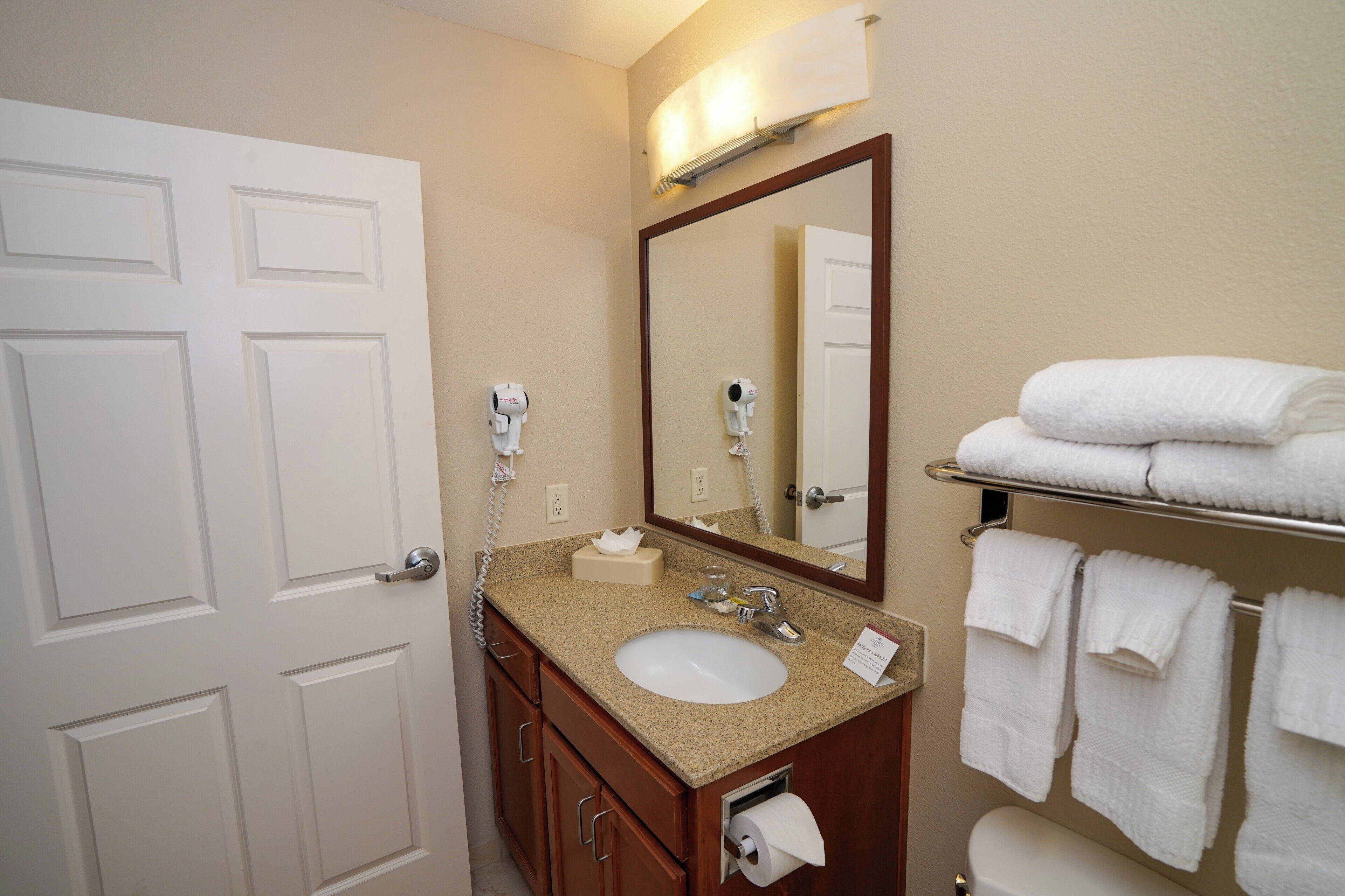 A hotel bathroom with a sink, mirror, towel rack, and toilet.